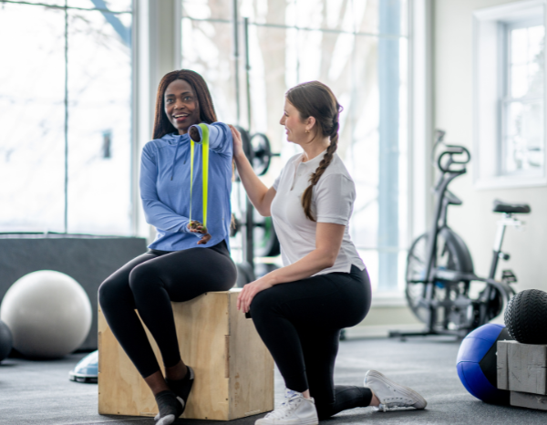 A Physical Therapist helps a woman missing an arm perform physical therapy exercises.