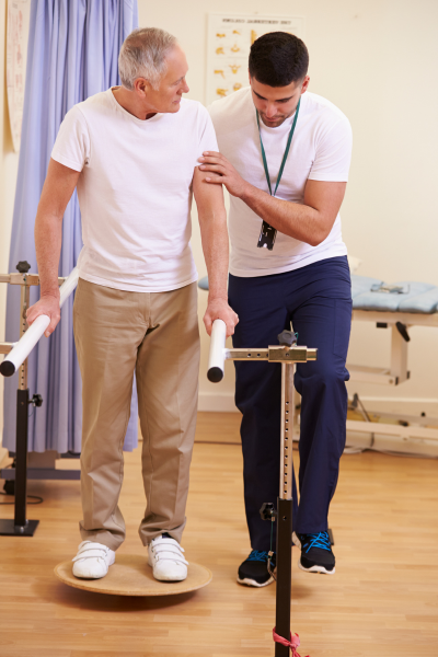 A Phsyical Therapist helps an older man balance on a Bosu ball